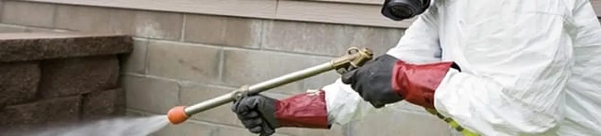 Pest control technician applying exterior insect treatment along a home foundation in Colorado Springs, CO