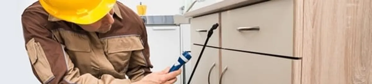 Roach exterminator applying treatment under kitchen cabinets in Colorado Springs, CO