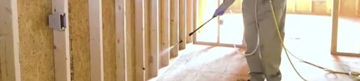 Termite treatment technician applying spray along framing and unfinished walls in Colorado Springs, CO